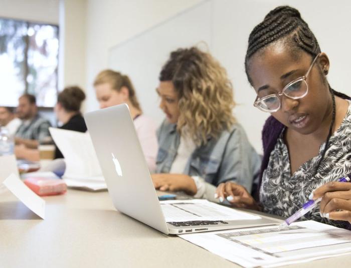 专业的MBA学生坐在一排课桌前，用笔记本电脑和纸做作业